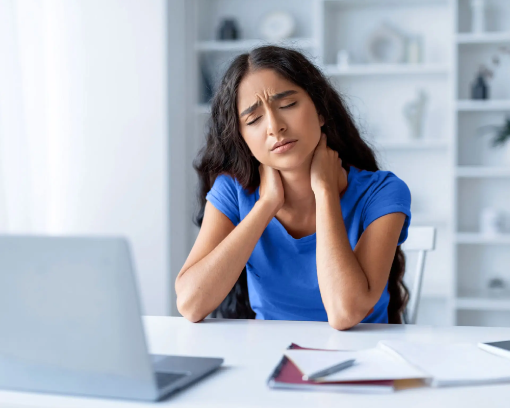 Mujer con dolor de cuello frente al portátil.